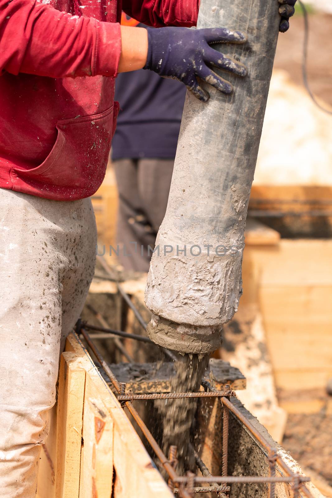 Close up of construction worker laying cement or concrete into the foundation formwork with automatic pump by Len44ik