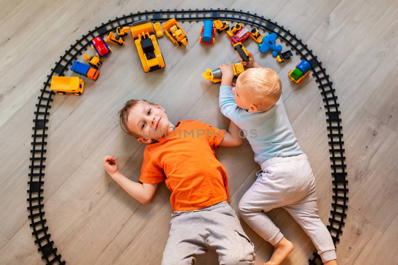 Preschool boys drawing on floor on paper, playing with educational toys - blocks, train, railroad, vehicles at home or daycare. Toys for preschool and kindergarten. Top view.