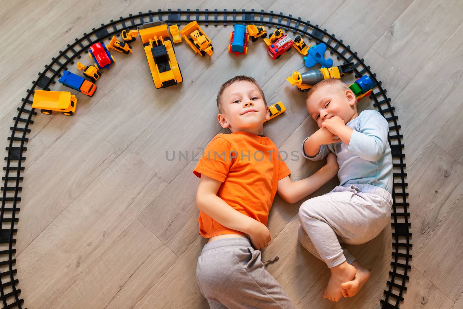 Preschool boys drawing on floor on paper, playing with educational toys - blocks, train, railroad, vehicles at home or daycare. Toys for preschool and kindergarten. Top view.