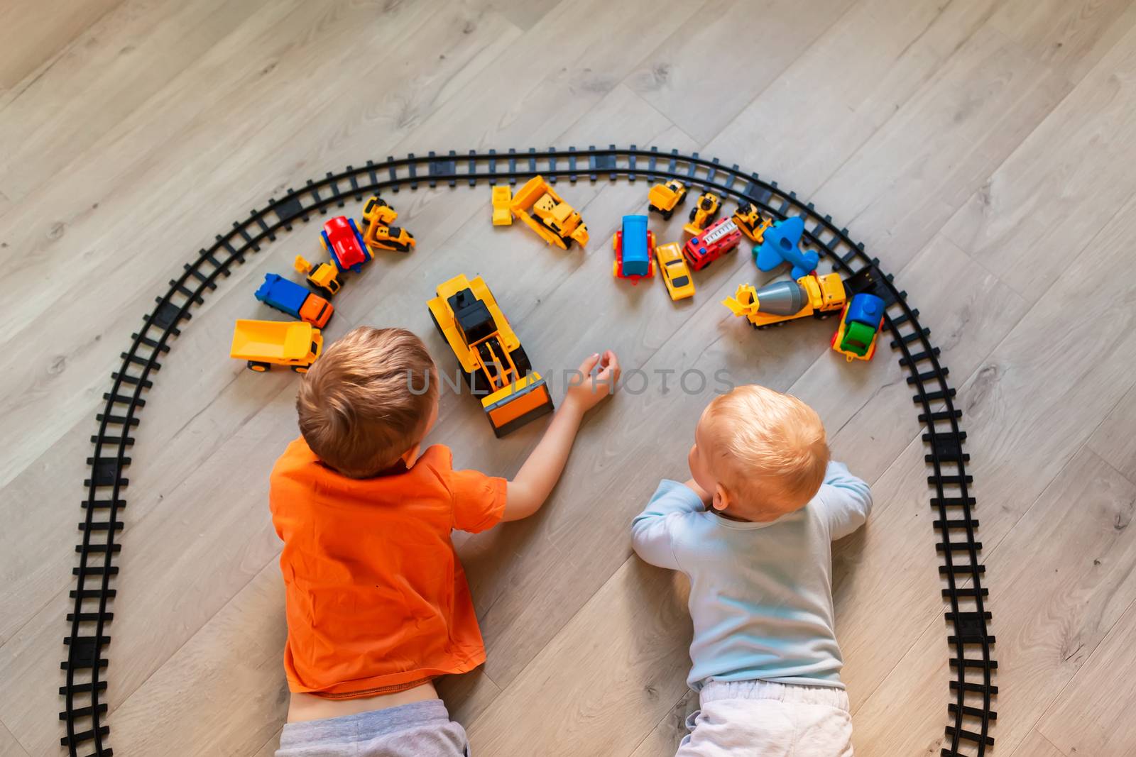 Preschool boys drawing on floor on paper, playing with educational toys - blocks, train, railroad, vehicles at home or daycare. Toys for preschool and kindergarten. Top view.