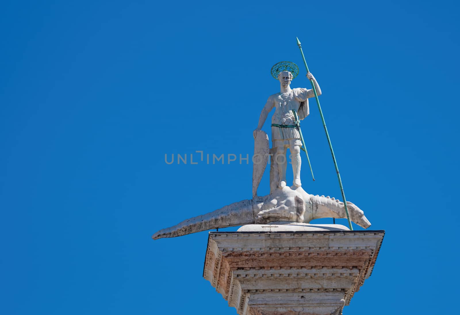 Saint Theodore medieval statue with bronze lance and shield trampling evil dragon, at the top of an ancient column erected in the 12th century in Venice