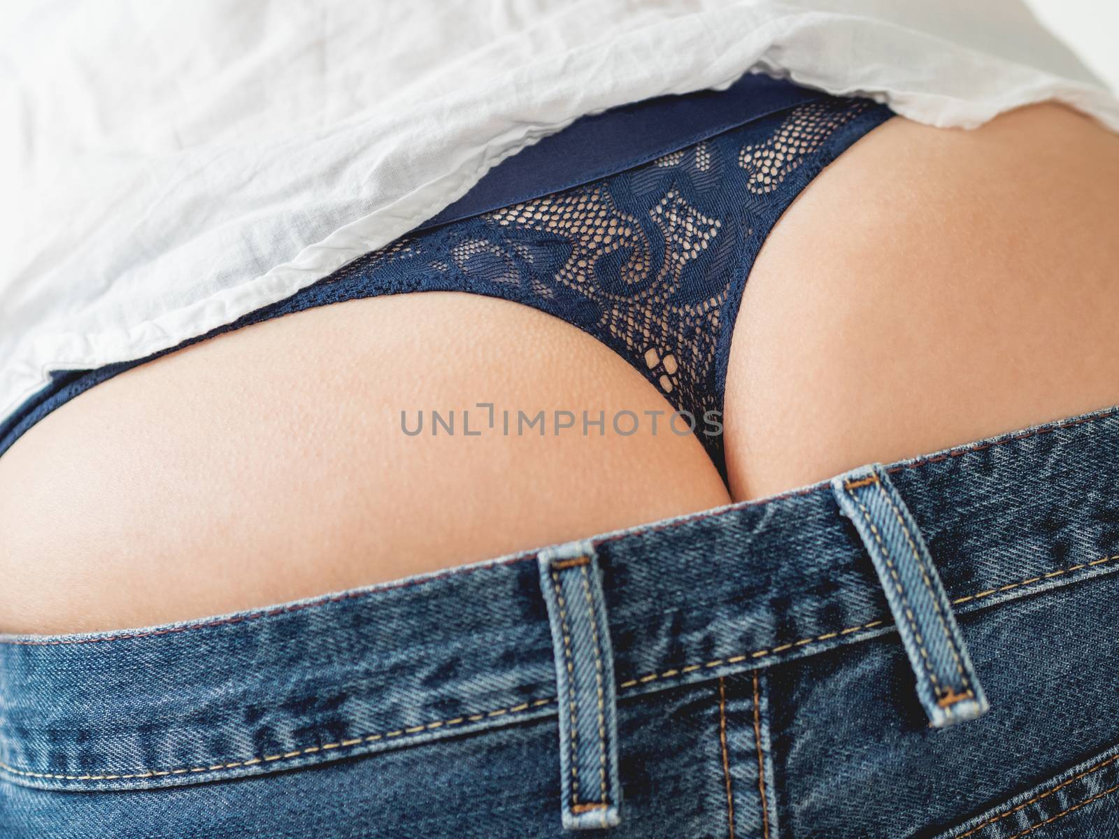 Close up photo of woman buttocks with laced thong and classic blue jeans. Woman in white shirt and underwear.