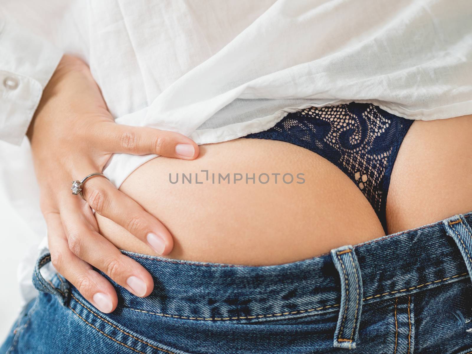 Close up photo of woman buttocks with laced thong and engagement ring on her finger. Woman in white shirt, classic blue jeans and underwear.