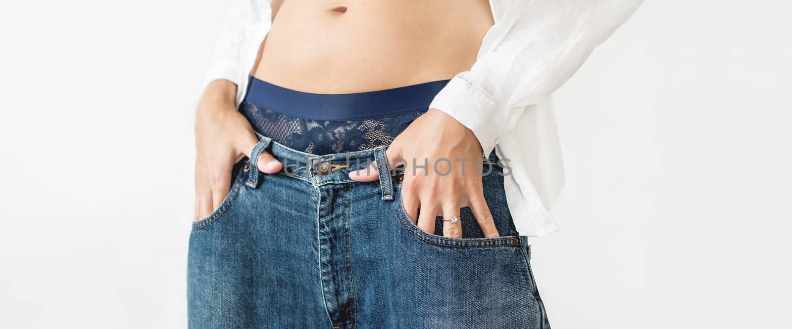 Woman hides her palm with engagement ring in pocket of classic blue jeans. Modern fashion - low rise boyfriend jeans and white shirt.