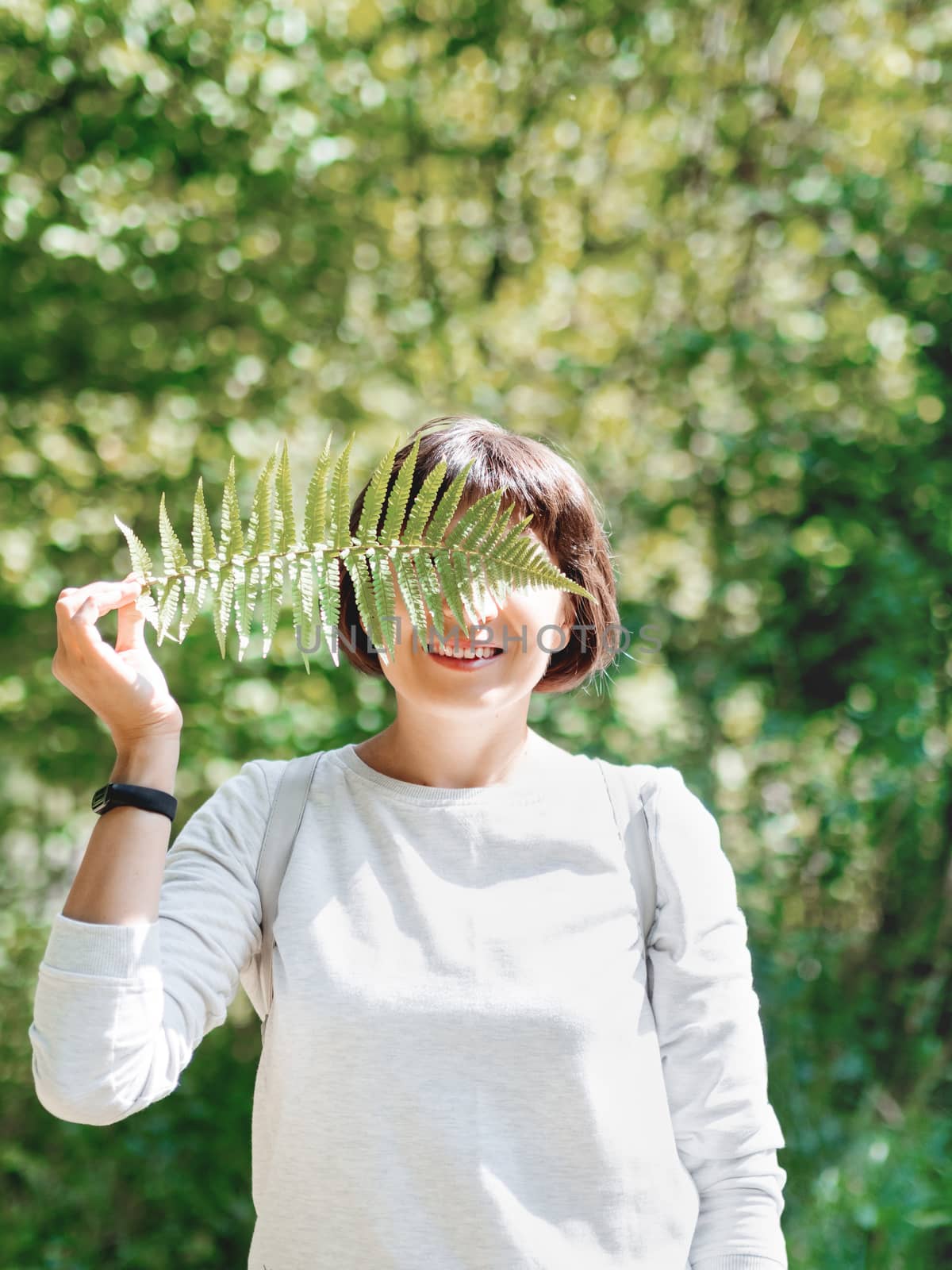 Young woman is hiding her eyes with fern leaf. Symbol of life, tranquility and unity with nature. Summer in forest.