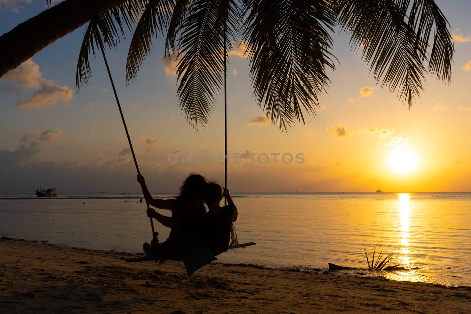 Silhouetted couple in love walks on the beach during sunset. Riding on a swing tied to a palm tree and watching the sun go down into the ocean by Try_my_best