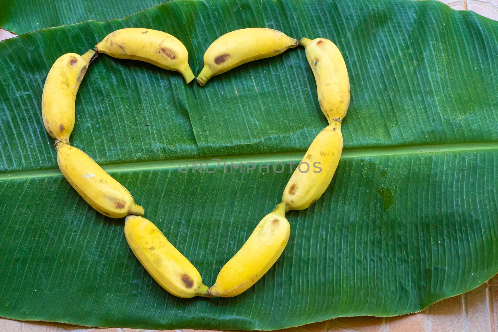 Flat lay layout of yellow bananas in the form of a heart on a green banana leaf. Eco food.