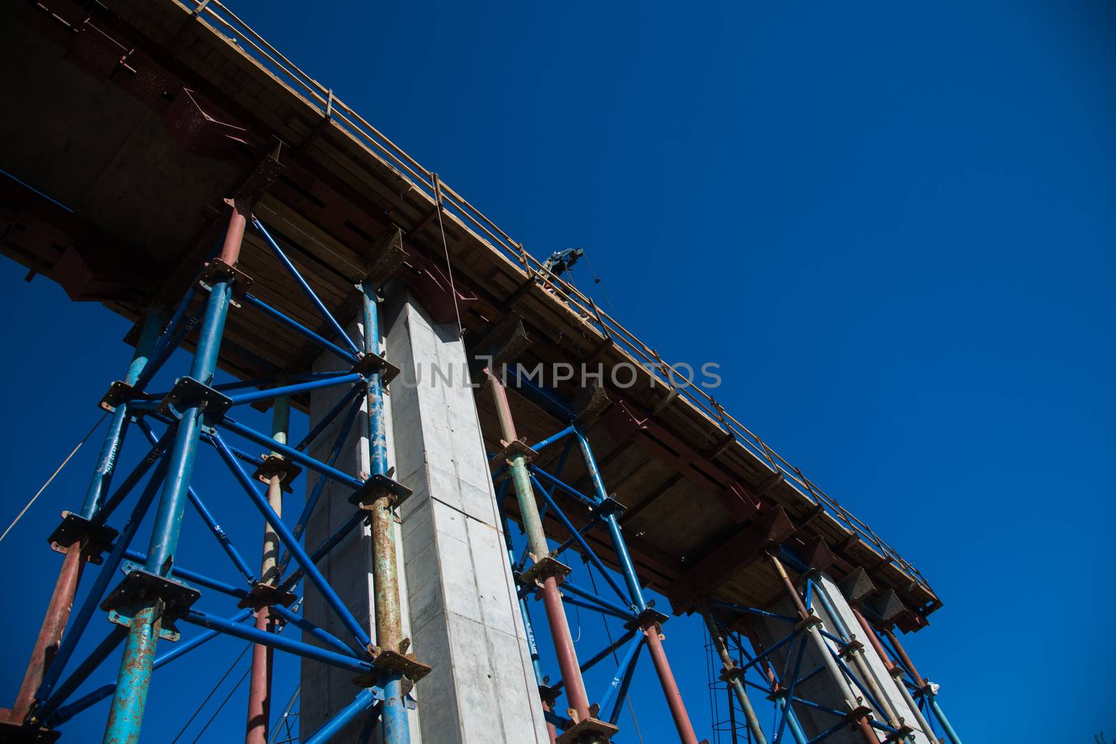 Construction of the interchange of a road bridge across the river. Builders and construction equipment on the construction site. The support of the bridge against the blue sky.