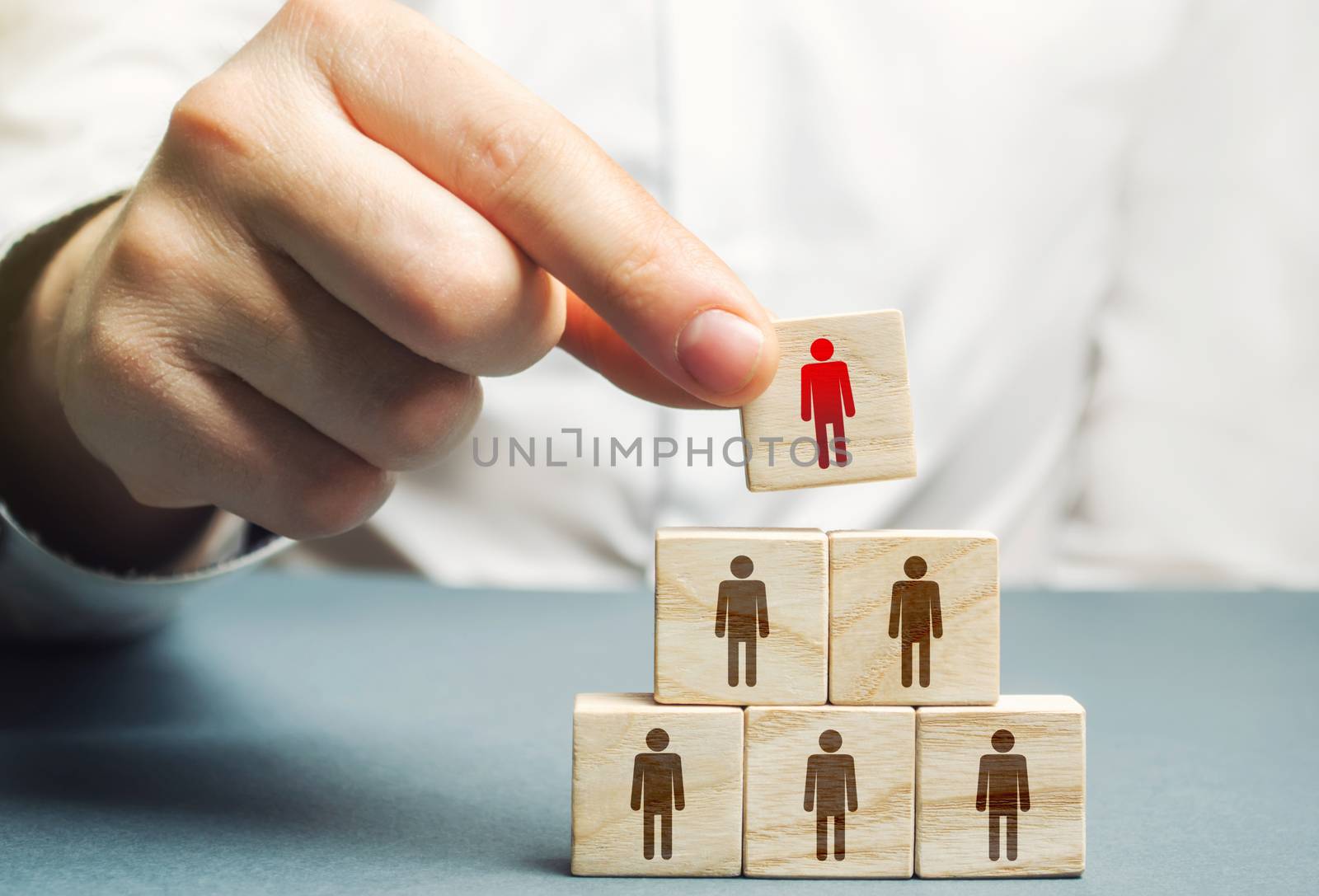 A hand places a mentor leader at the head of a group of people. Team building, hierarchical power vertical. Leadership skills. Teamwork, cooperation and collaboration. Management of effective team.