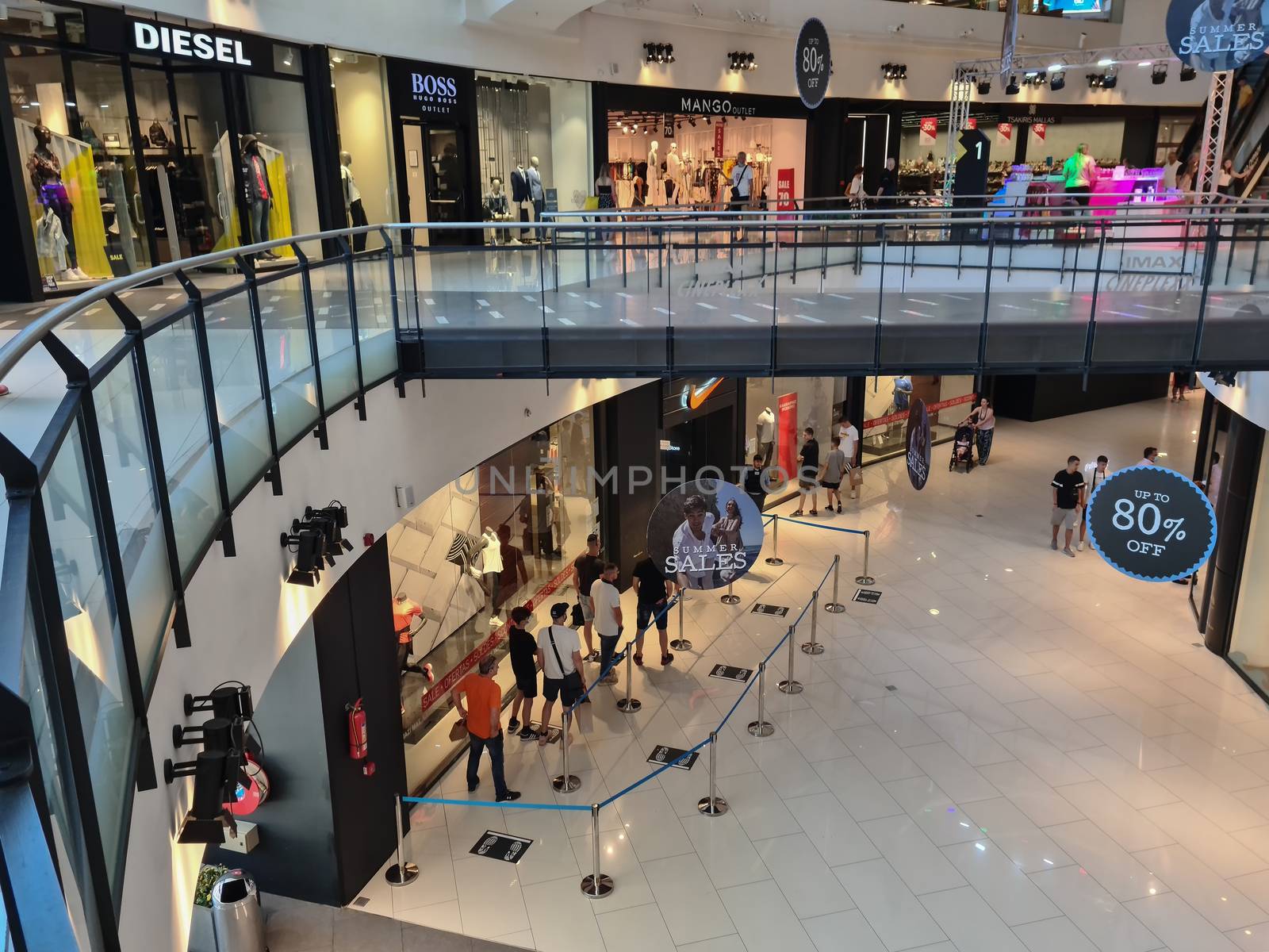 Unidentified people keep their distance outside shop at One Salonica Outlet, during summer sales.