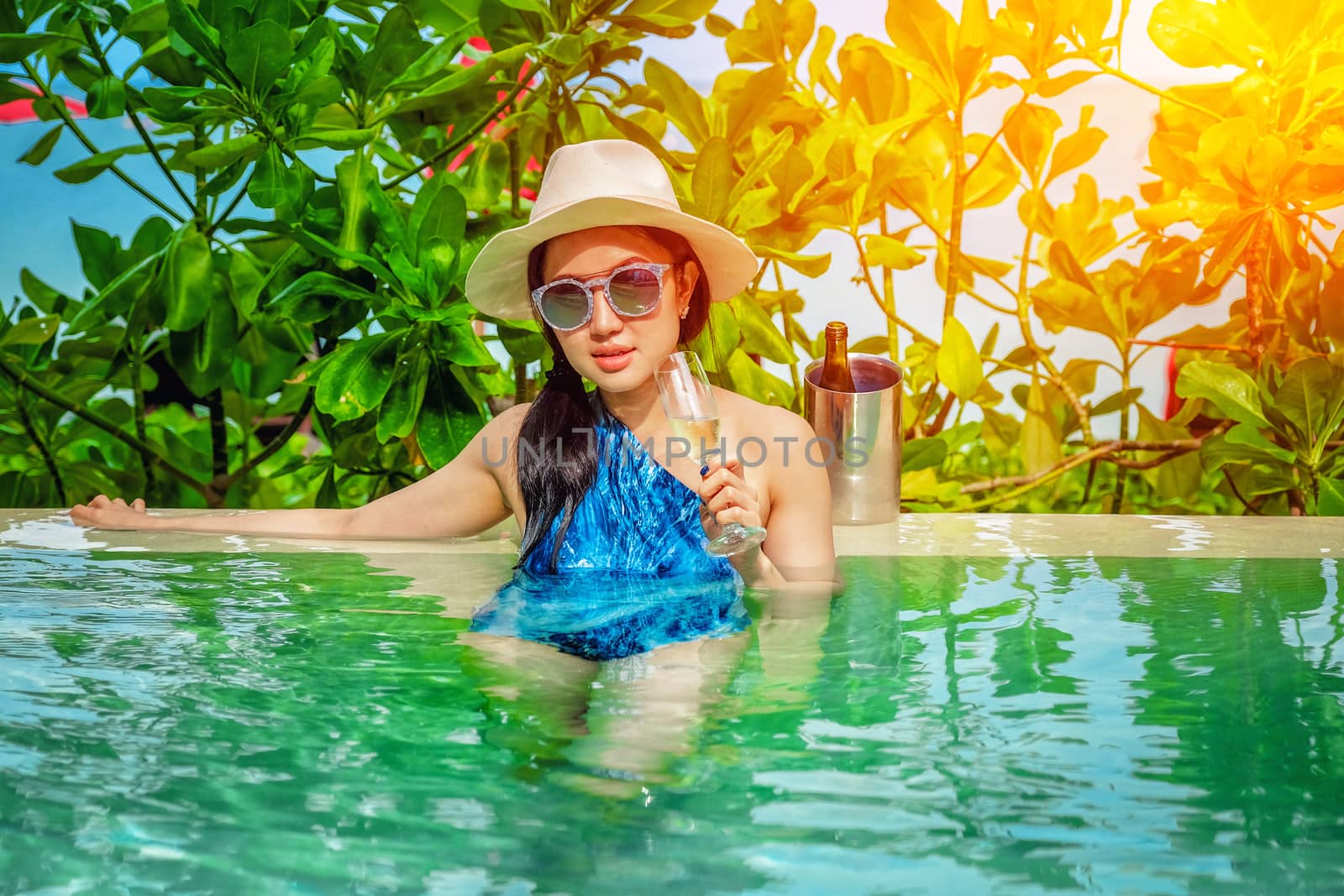 Beautiful young woman in swimming pool with a champagne in her hands