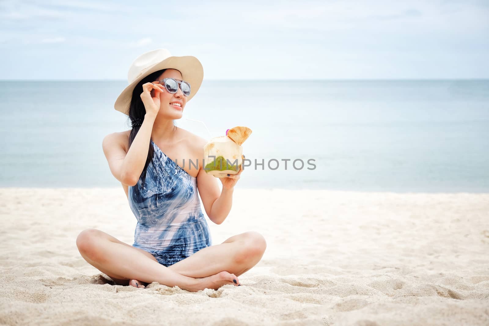 Happy woman with fresh coconut water on the beach by Surasak