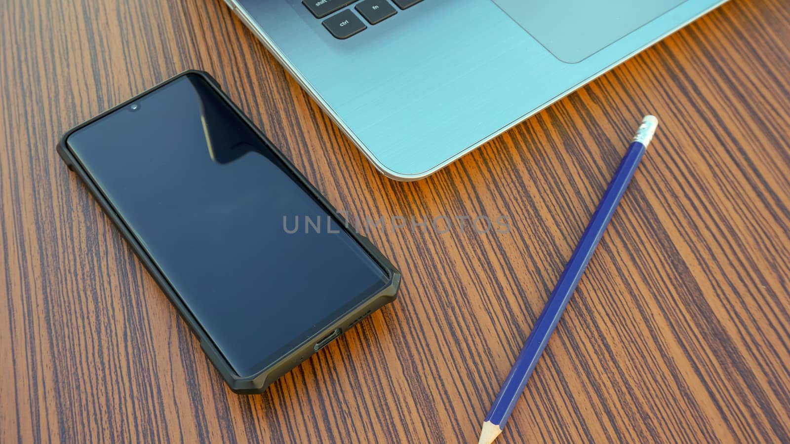 Computer notebook with black smartphone and a blue pencil on a wooden desk.