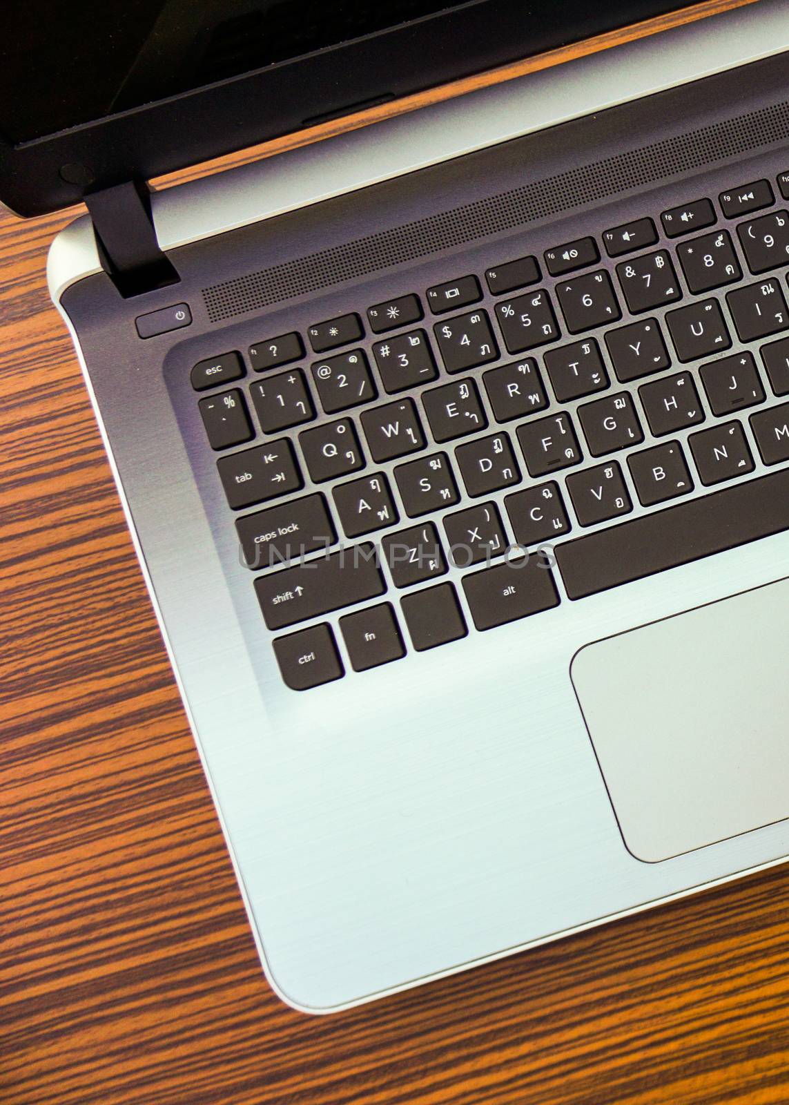 A laptop computer with English and Thai keypad on a wooden design working table.