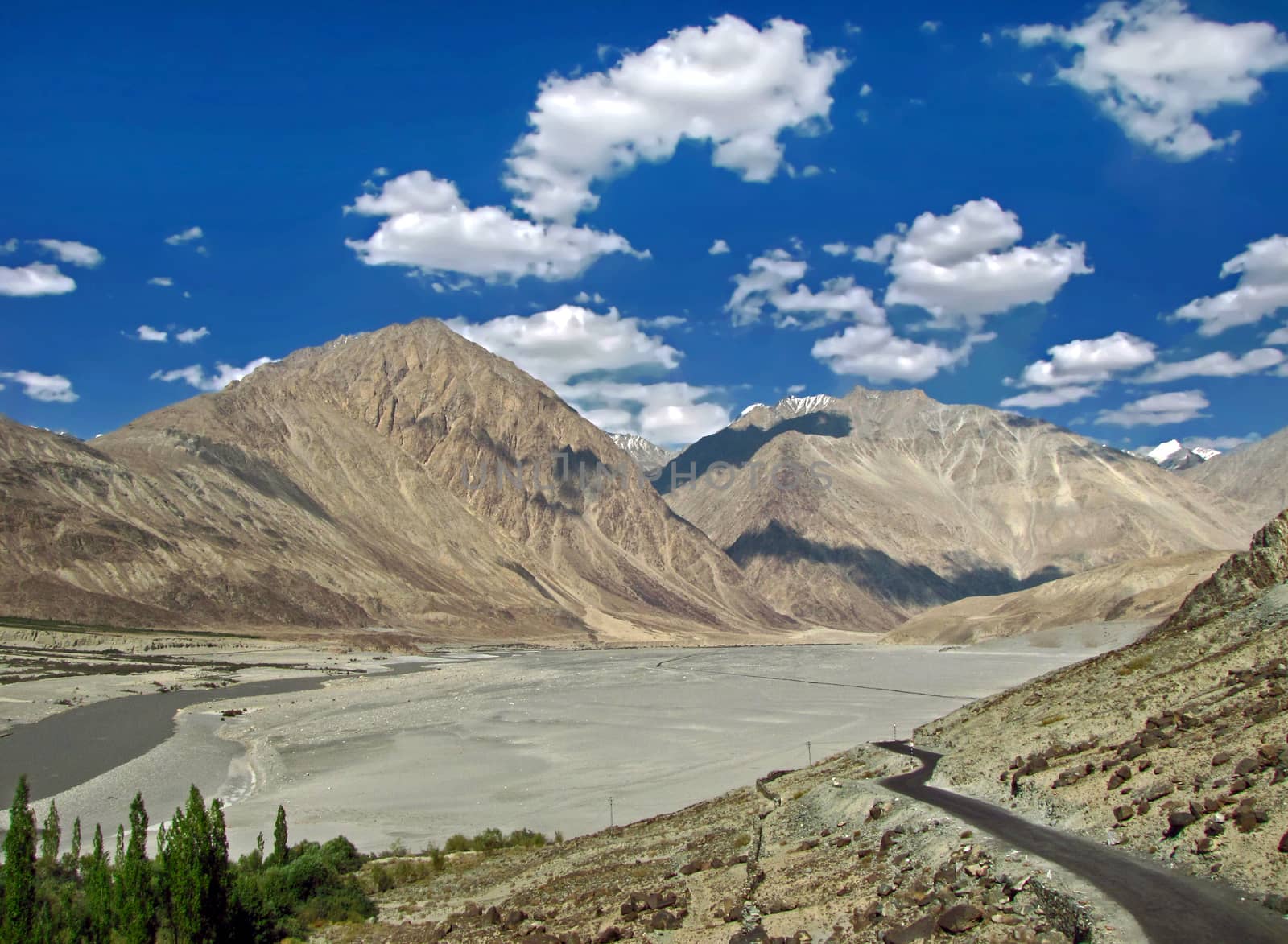 Lonely road on backdrop of beautiful mountain and blue sky on way to Diskin in Nubra valley, Ladakh, india. by lalam