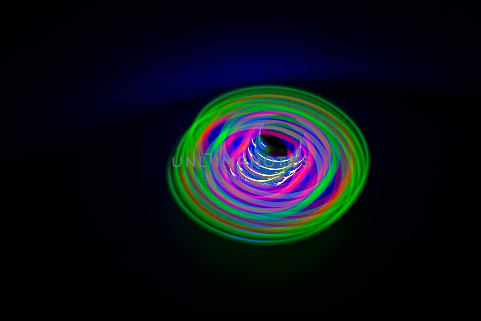 Long exposure, slow shutter, multicolor Led light painting of a spinning top on abstract dark black background.