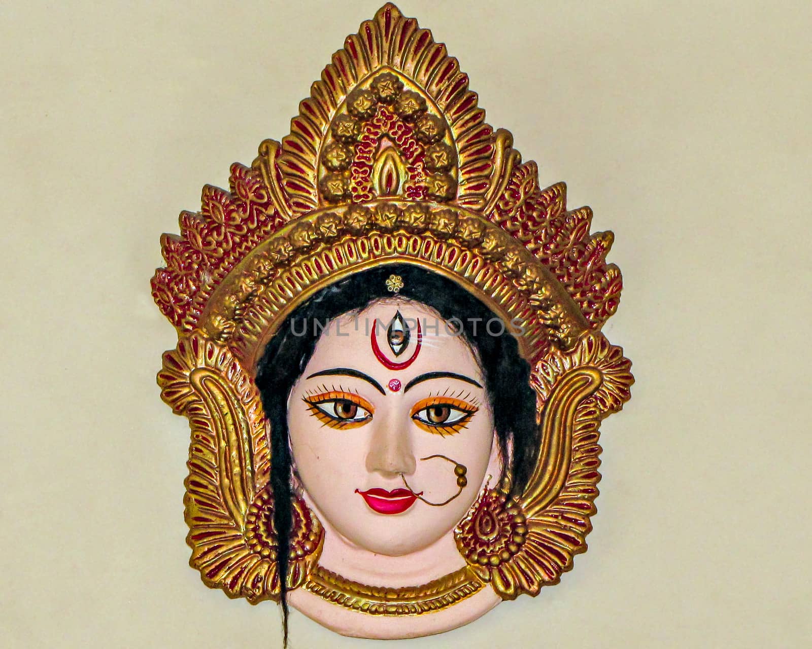Precisely crafted, painted and decorated face of Godess Durga , hanging on a wall. by lalam