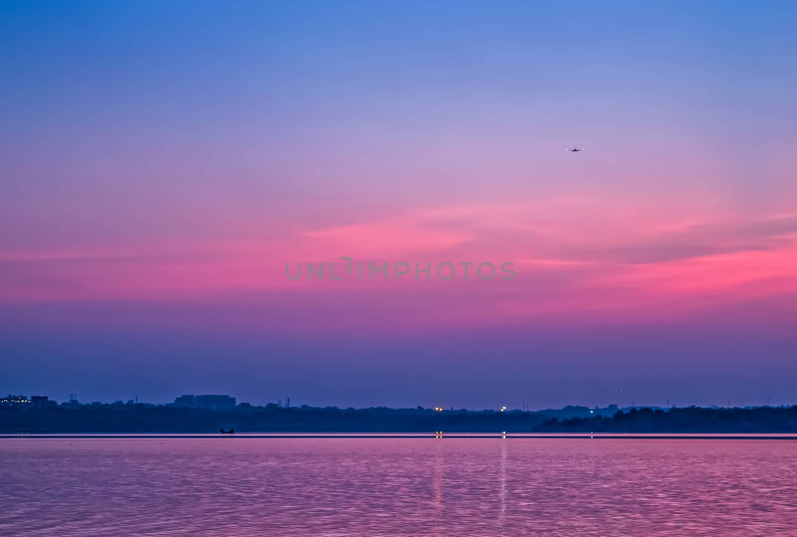 An aircraft approaching airport glides over Ambazari lake, Nagpur  with a backdrop of Sunset on a beautiful evening.Can be used as wallpaper. by lalam