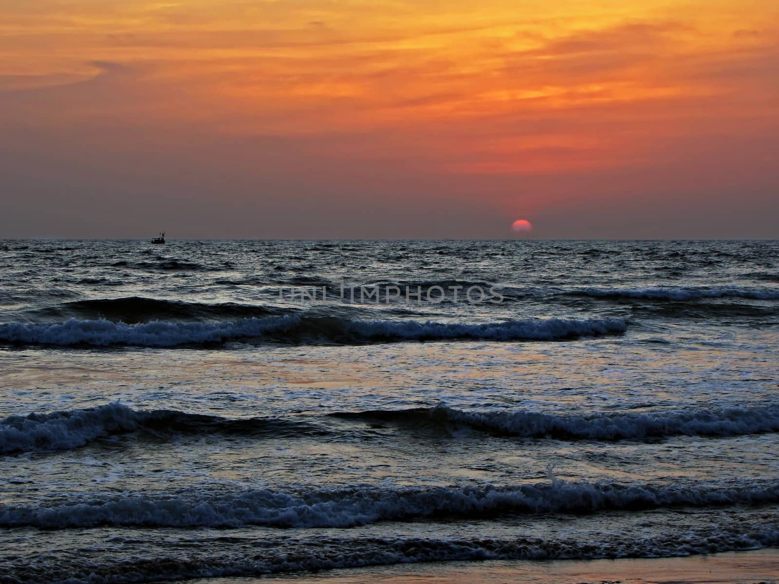 A small boat sailing in the sea with waves on a background of beautiful Sunset.