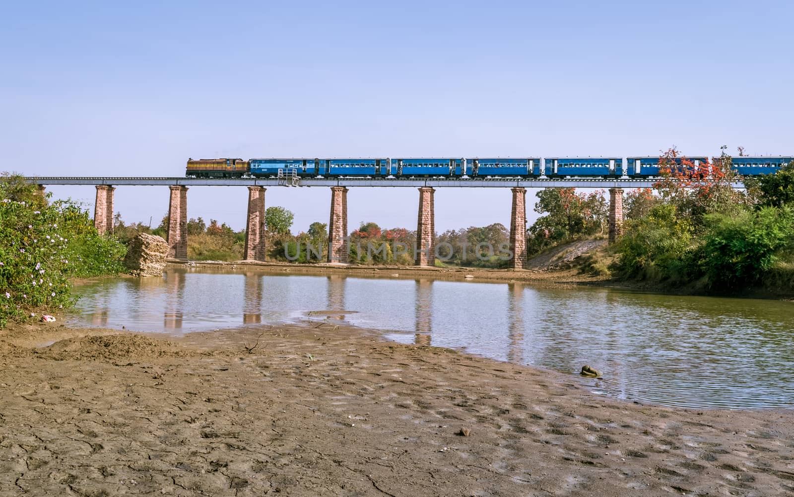 Narrow gauge train crossing Marhu river bridge with river. by lalam
