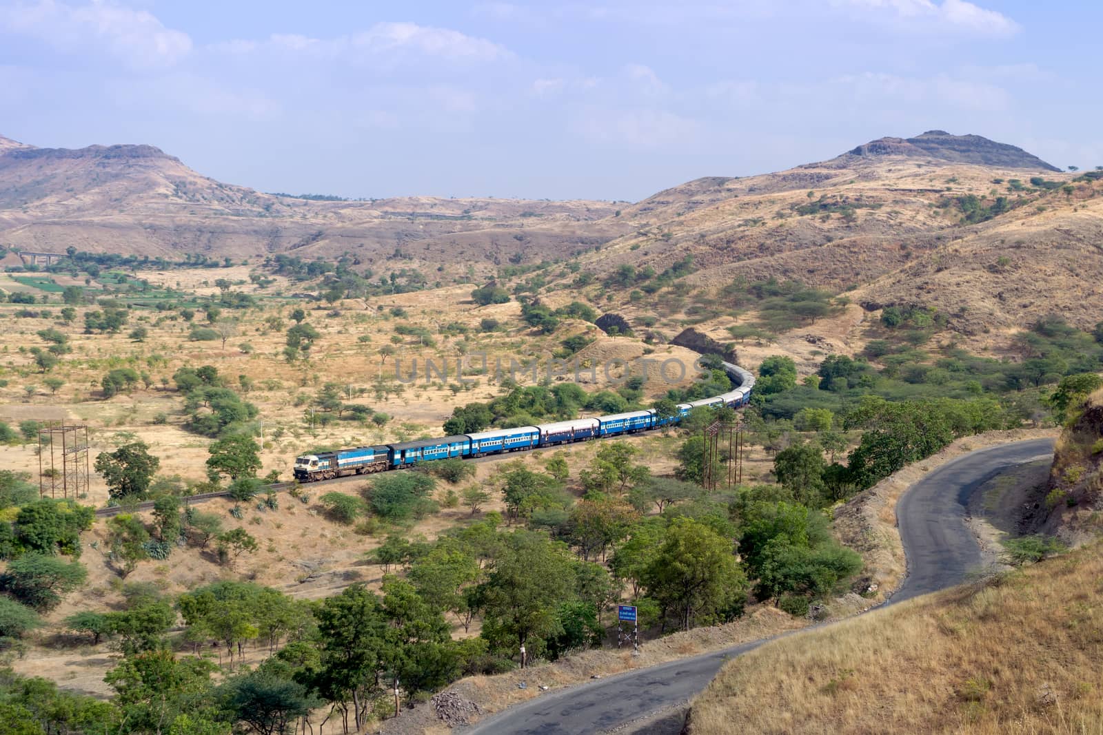 Train on a curved track with background of hills and sky and a foreground road. by lalam
