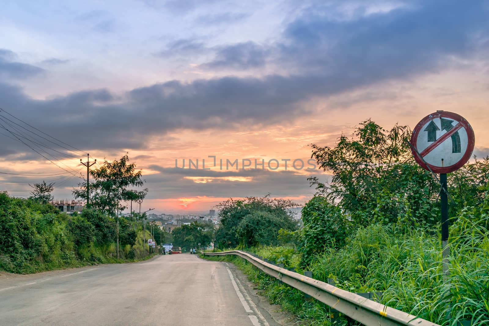 Beautiful Sunrise on a road going down the slope with 'no overtake' signboard.