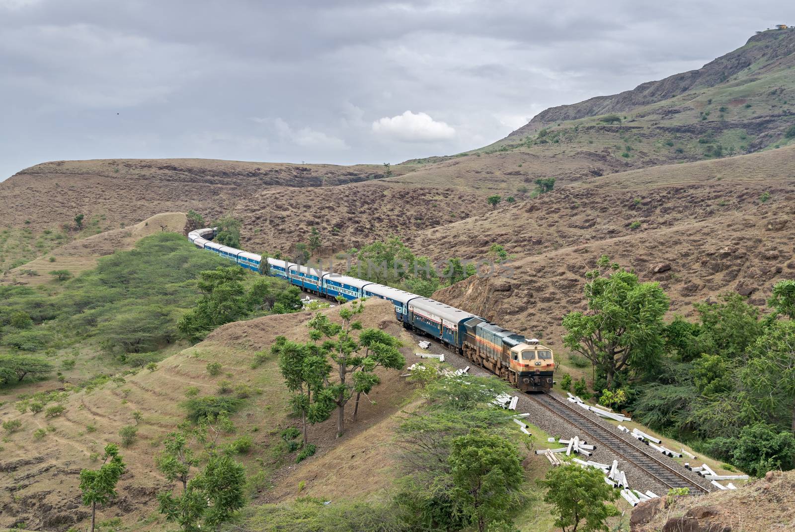 Train coming out of a hill cutting with background of mountains and clouds. by lalam