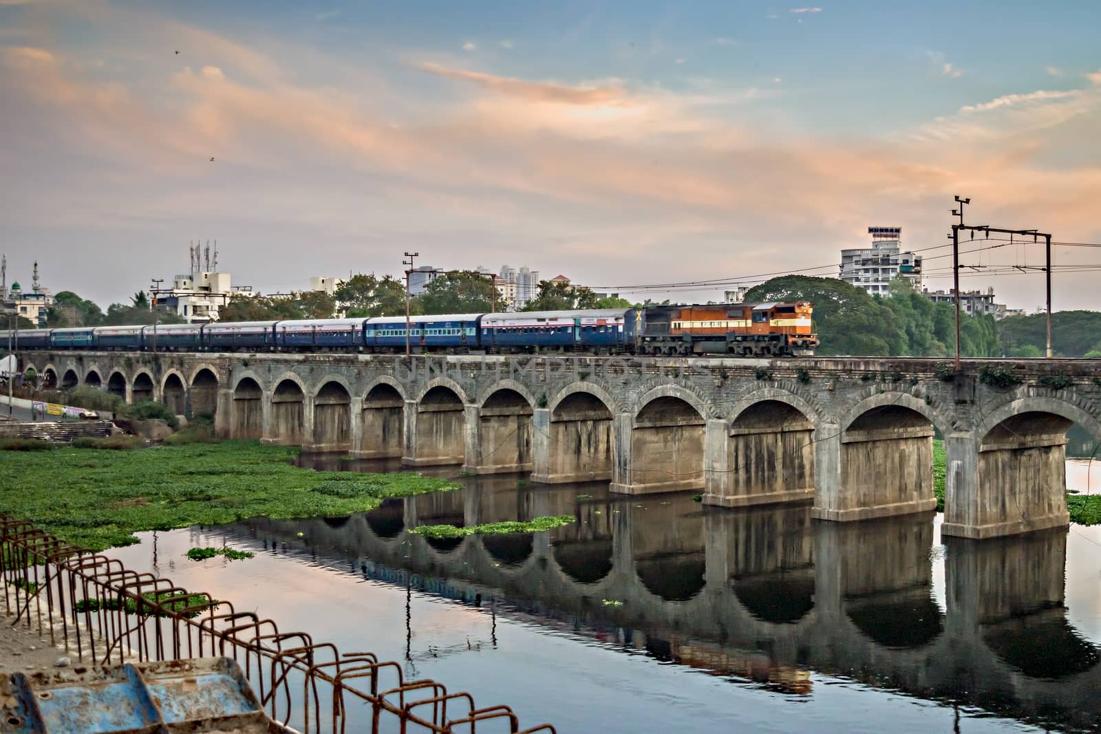Train passing over an old bridge named Sangam bridge, with nice reflection in water in Pune, Maharashtra. by lalam