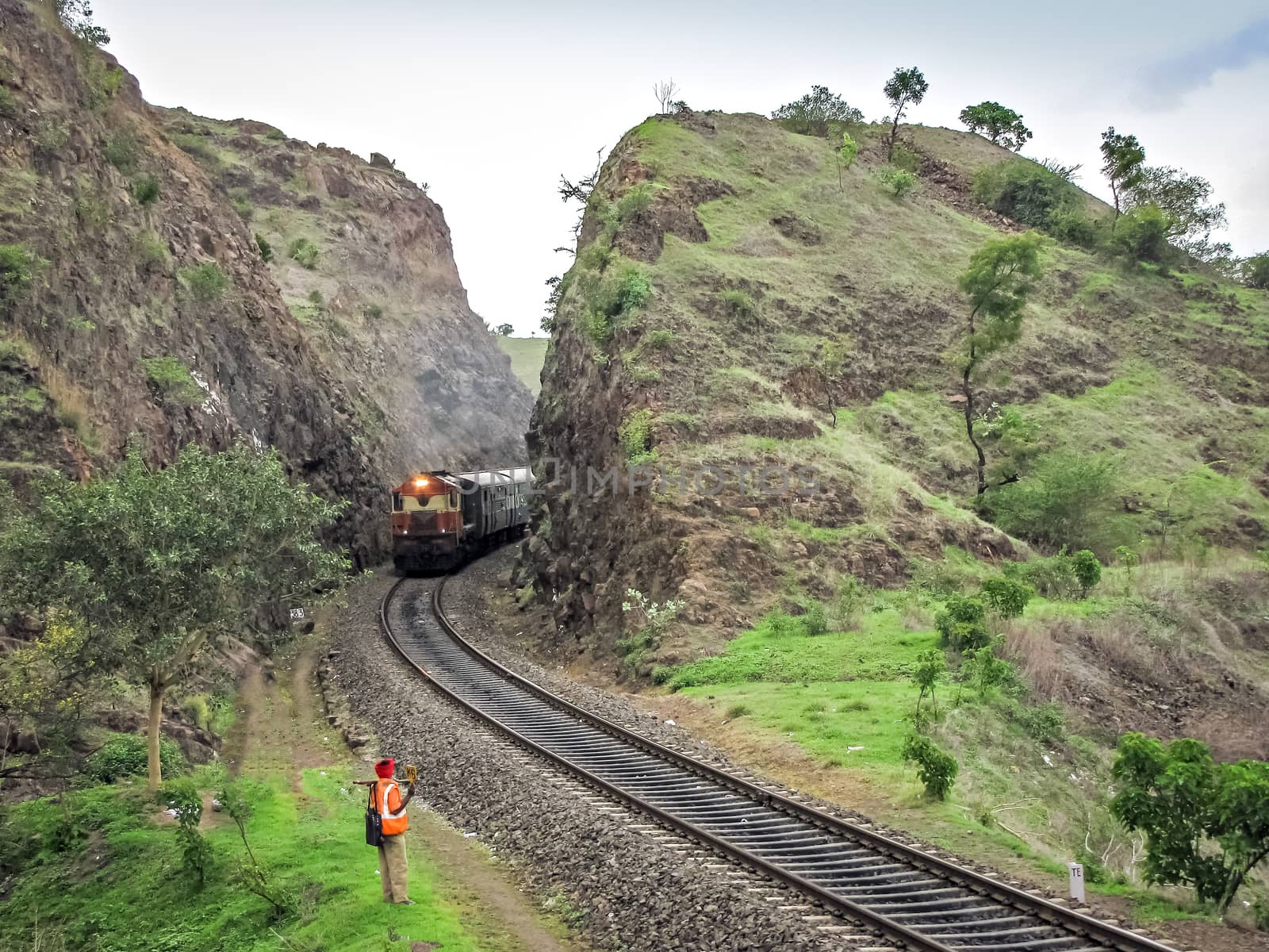 Diesel locomotive hauling a passenger train through a deep rock cutting in Shindawane, Maharashtra, India.