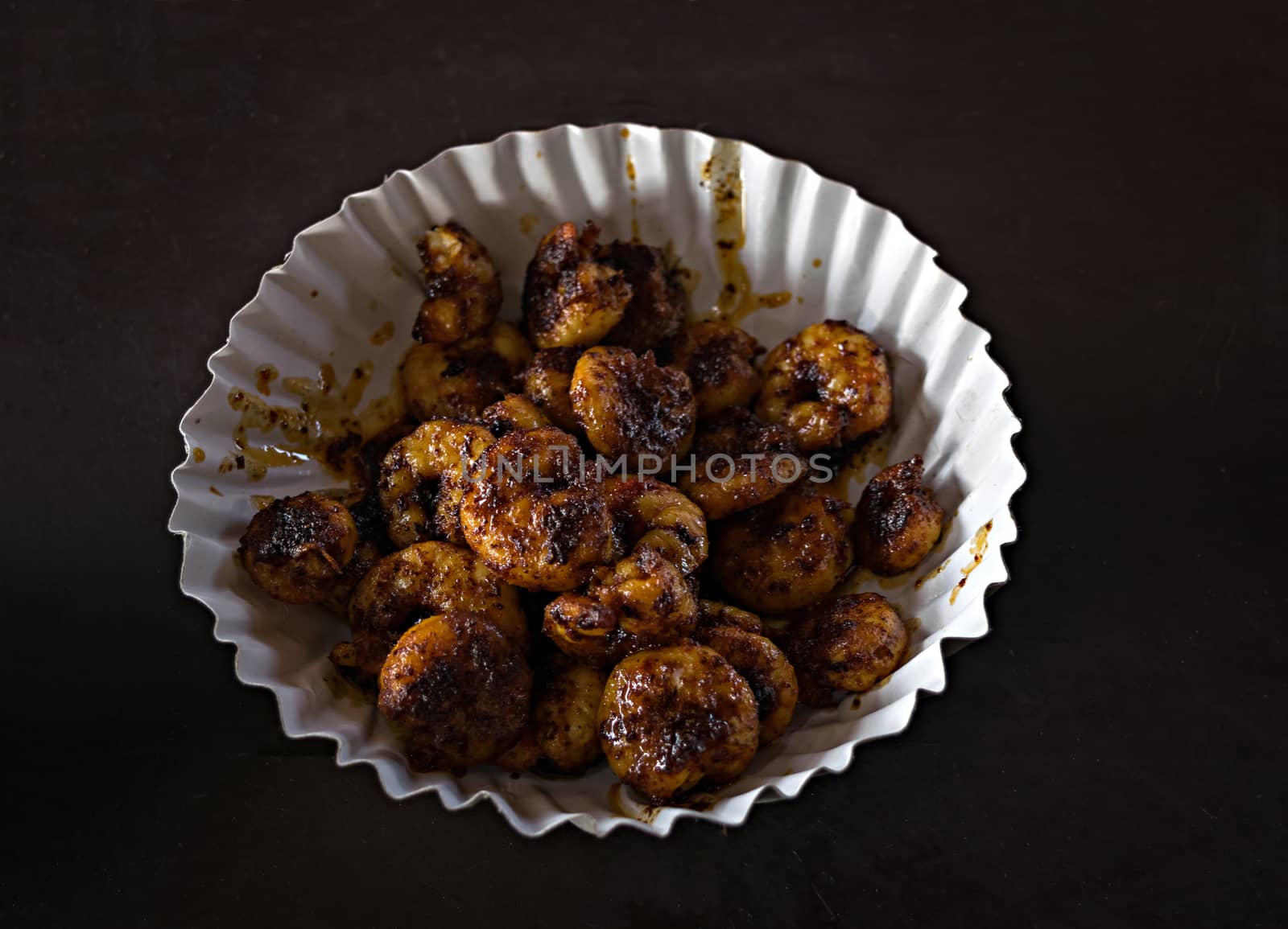 Freshly fried prawns ready to be served in a paper dish on a clear black background. by lalam