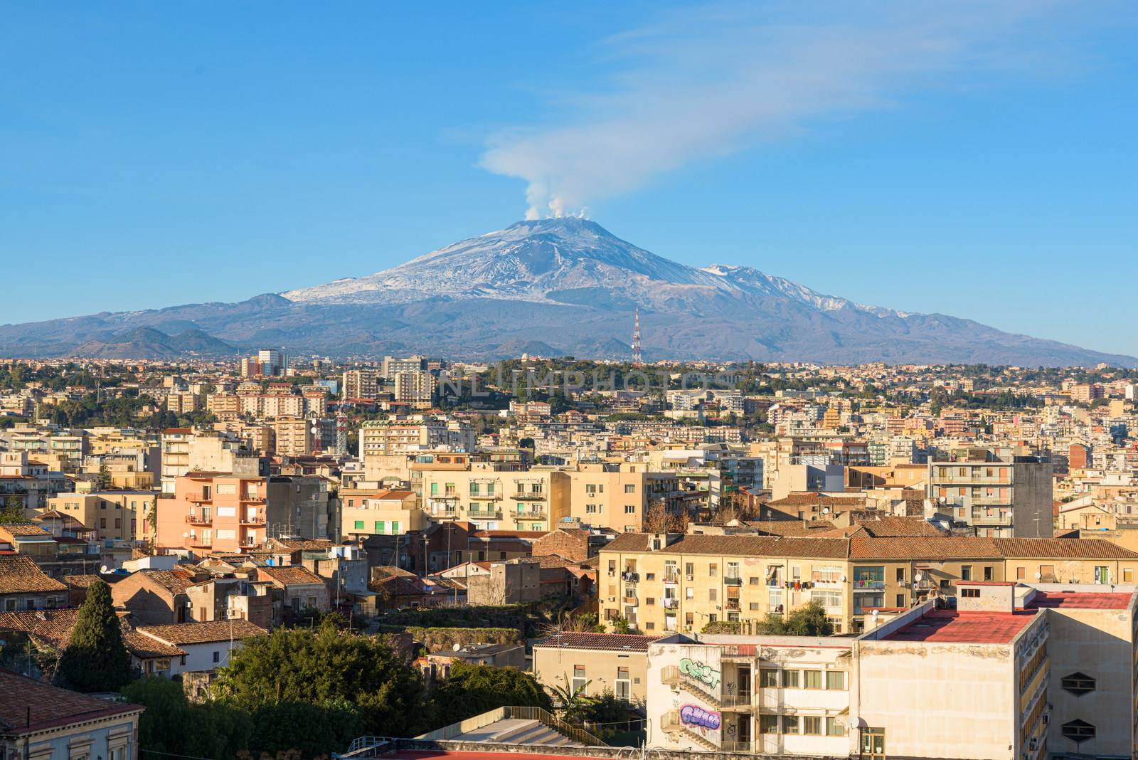 Mount Etna volcano erupts over the skyline and rooftops of medieval city center of Catania, Sicily, Italy