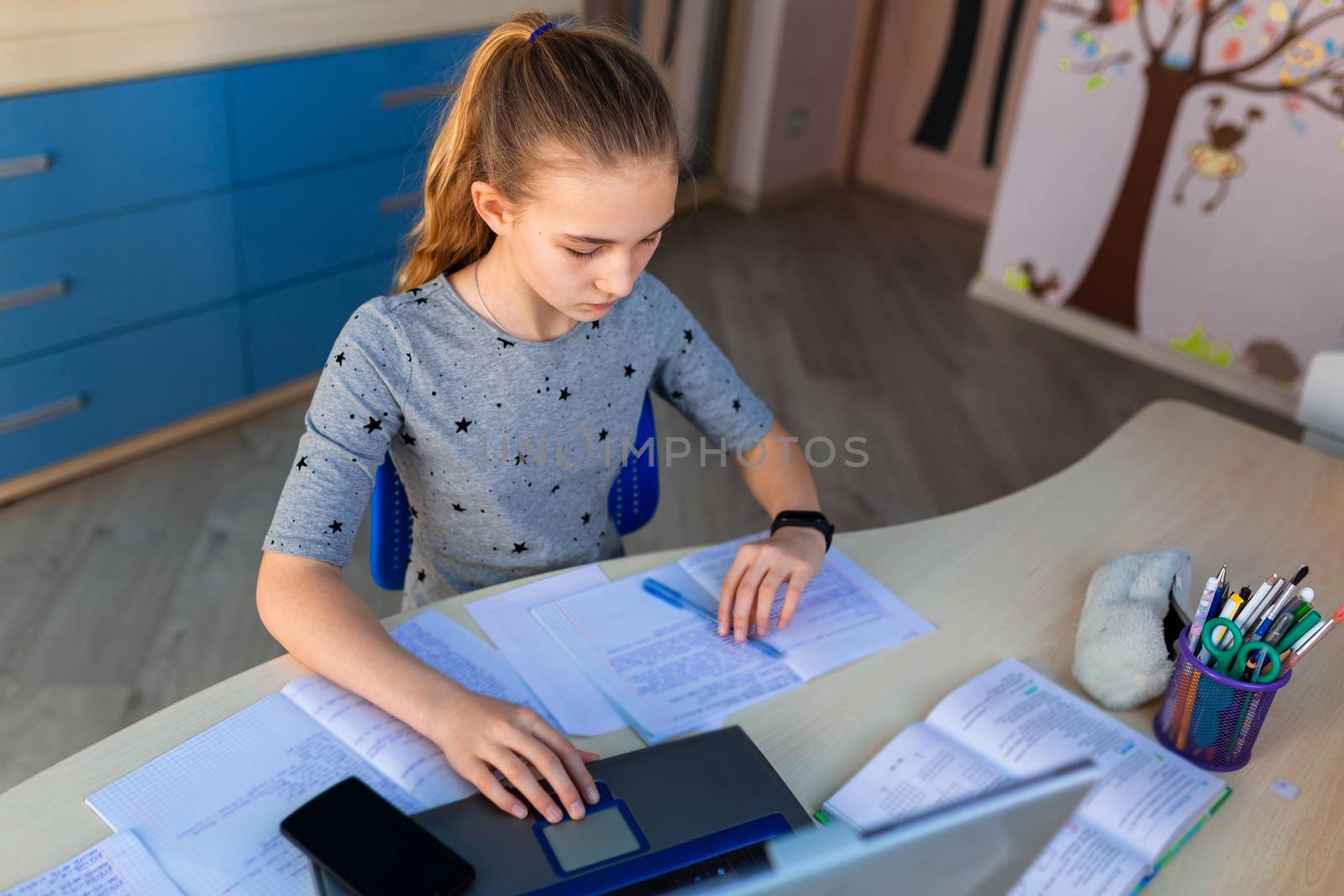 Beautiful young school girl working at home in her room with a laptop and class notes studying in a virtual class. Distance education and learning concept during quarantine by Len44ik