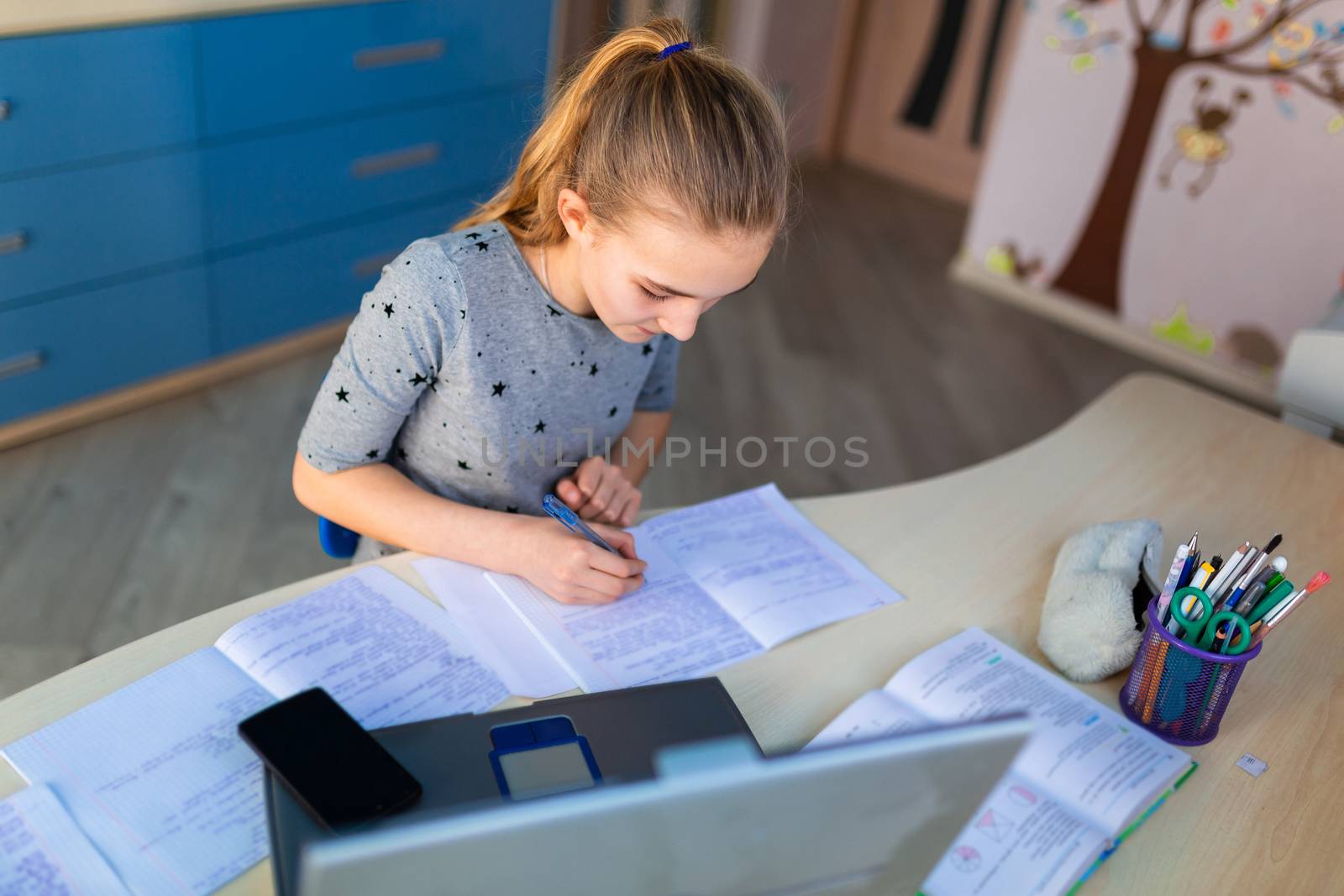 Beautiful young school girl working at home in her room with a laptop and class notes studying in a virtual class. Distance education and learning concept during quarantine by Len44ik