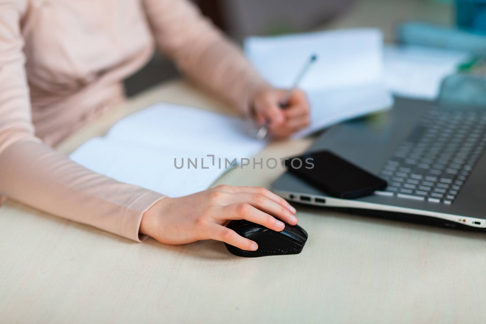 Close up of young school girl left-handed working at home in her room with a laptop and class notes studying in a virtual class. Distance education and online e-learning concept during quarantine