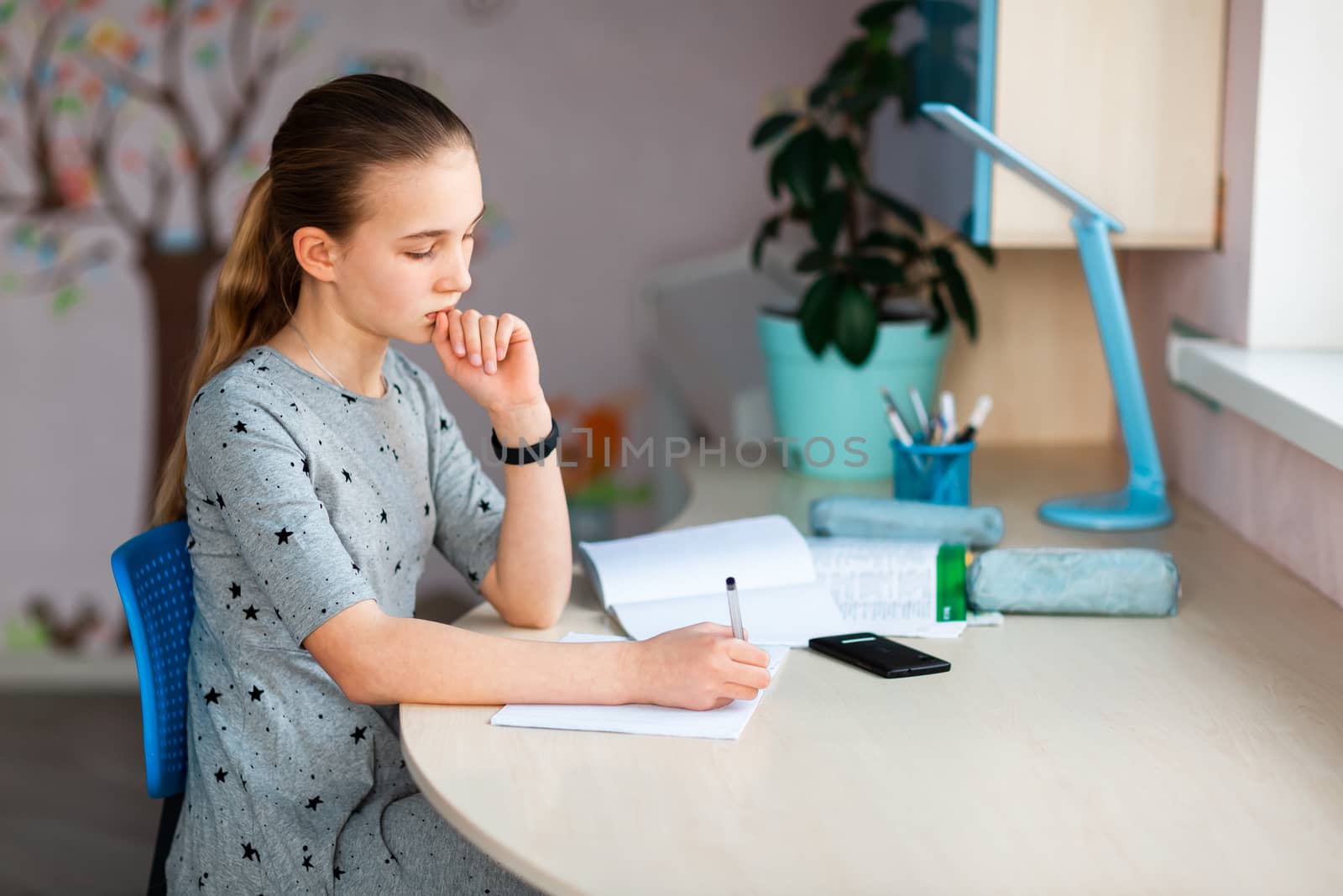 Beautiful young school girl working at home in her room with class notes and mobile phone and studying. Distance education and learning concept during quarantine
