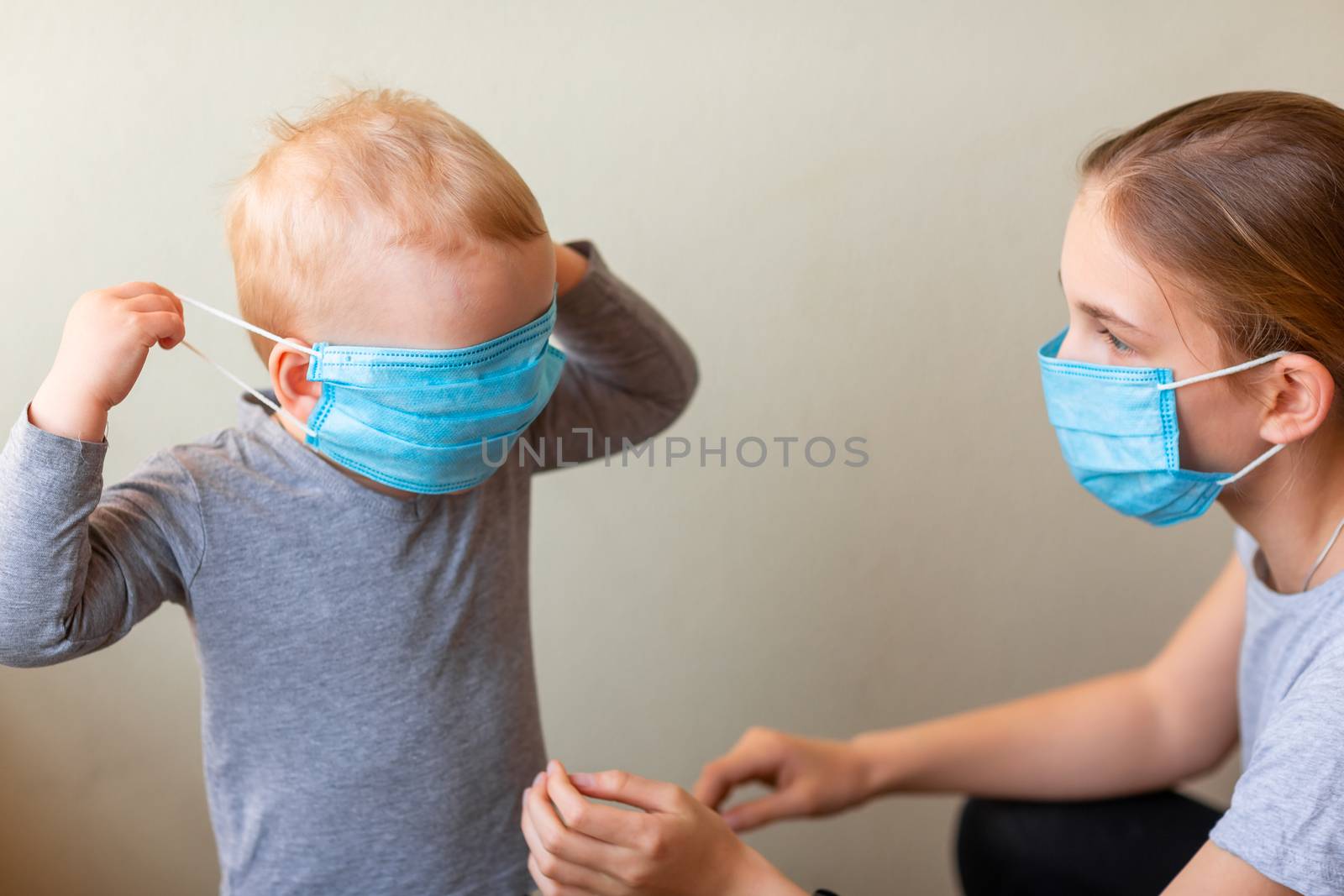 Teenage girl helping to his baby brother to wear a medical mask. Coronavirus protection, wearing masks concept