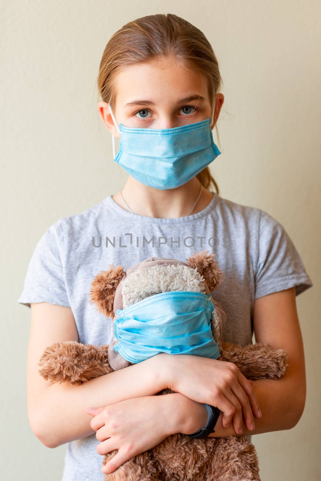 Little teenage girl with teddy bear toy both in medical masks sad and scared. Coronavirus protection, wearing masks concept