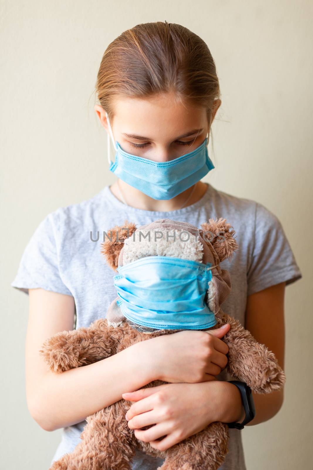 Little teenage girl with teddy bear toy both in medical masks sad and scared. Coronavirus protection, wearing masks concept