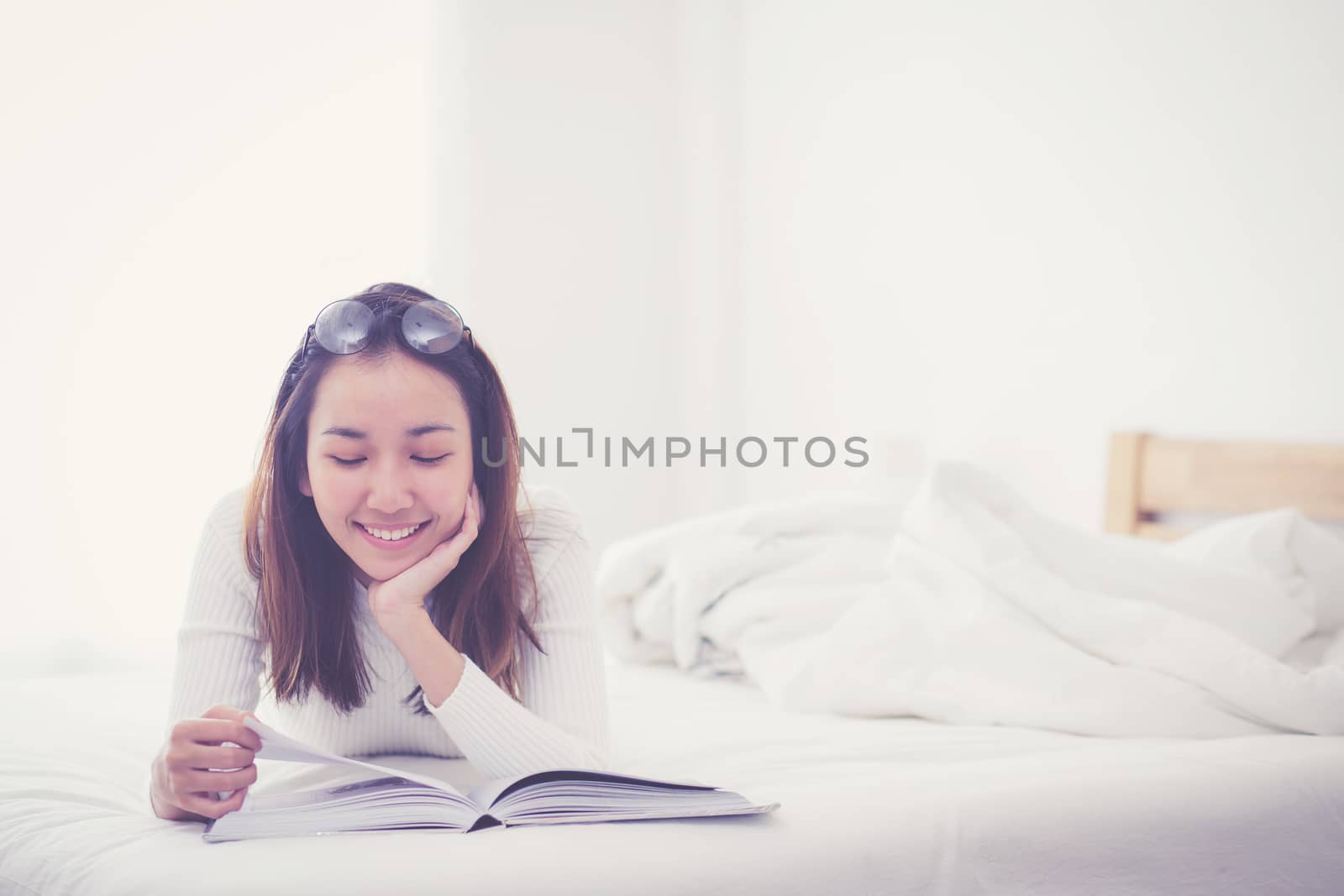 charming woman lying on bed reading a book in bedroom.