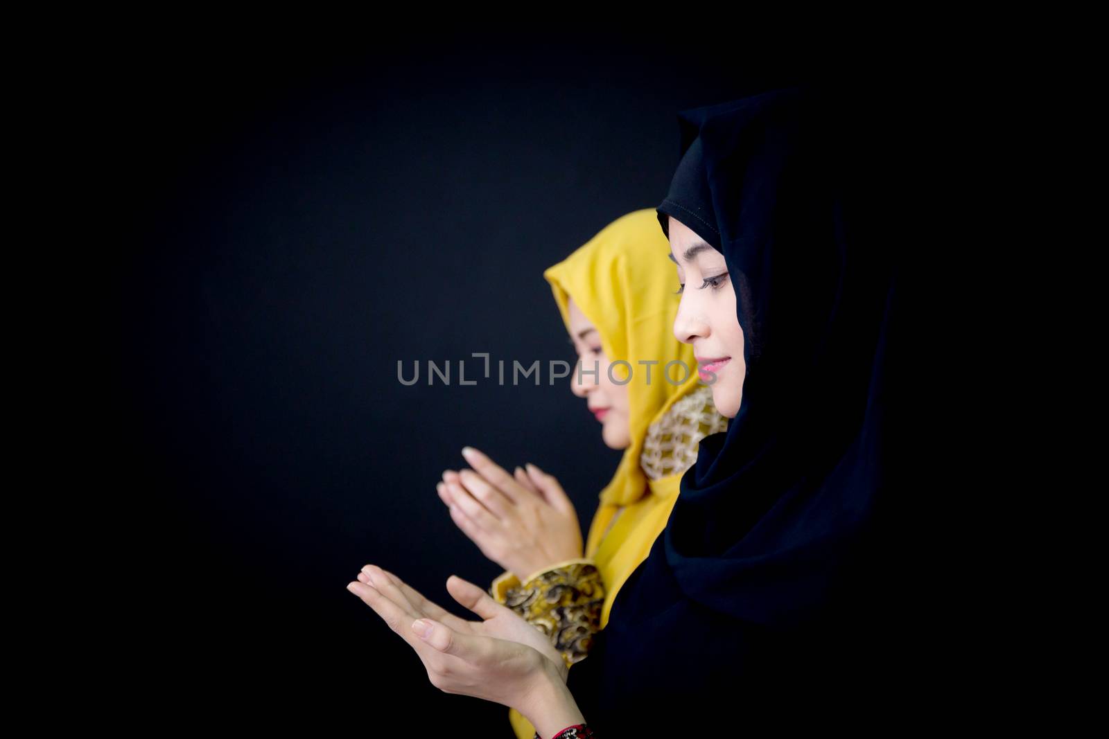 religious young Muslim two women praying over black background.