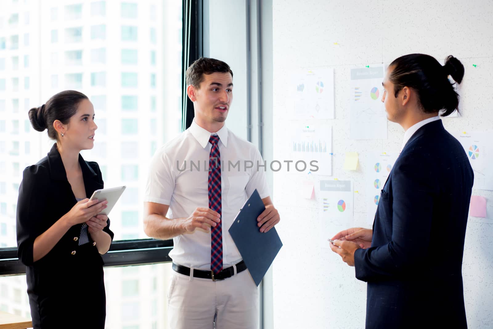 Three businesspeople standing in modern office looking file docu by nnudoo