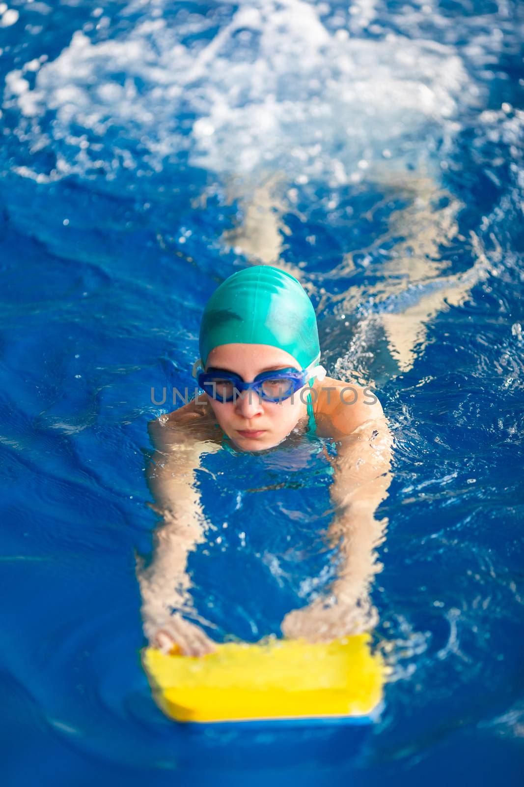 Cute little girl swimmer training in a swimming pool in glasses with a swimming kickboard. Swimming sport for kids concept