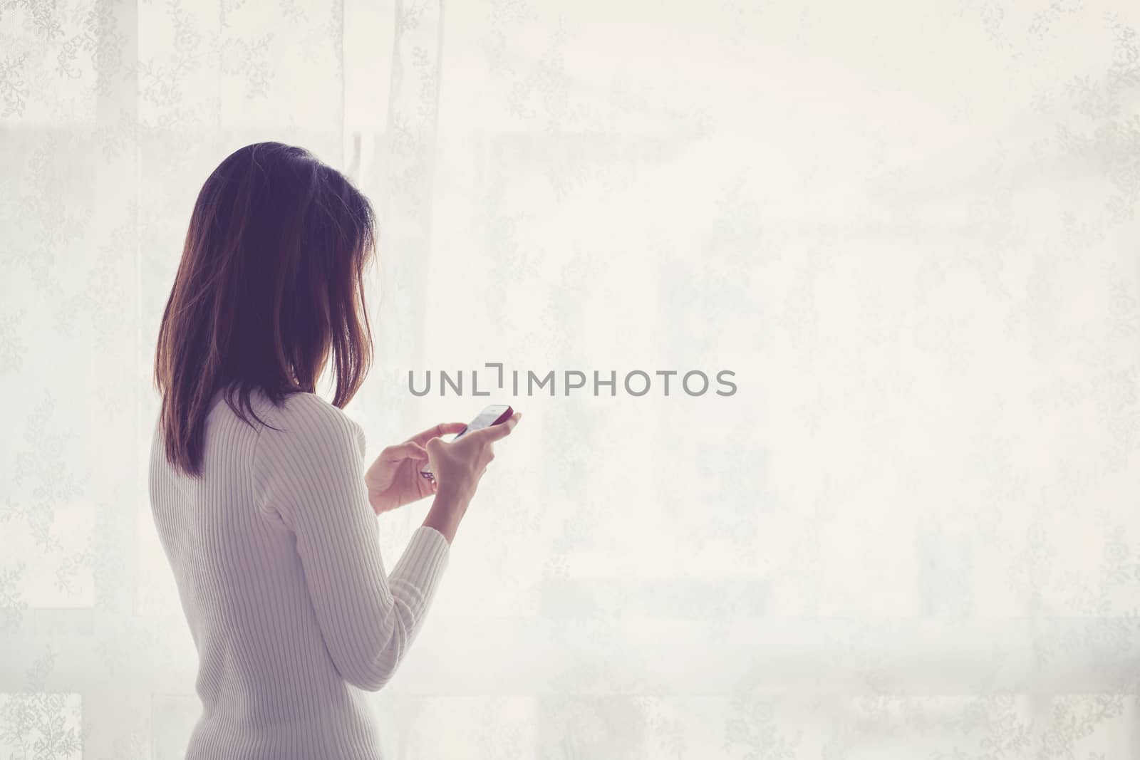 Beautiful young woman asian behind holding phone at a window.
