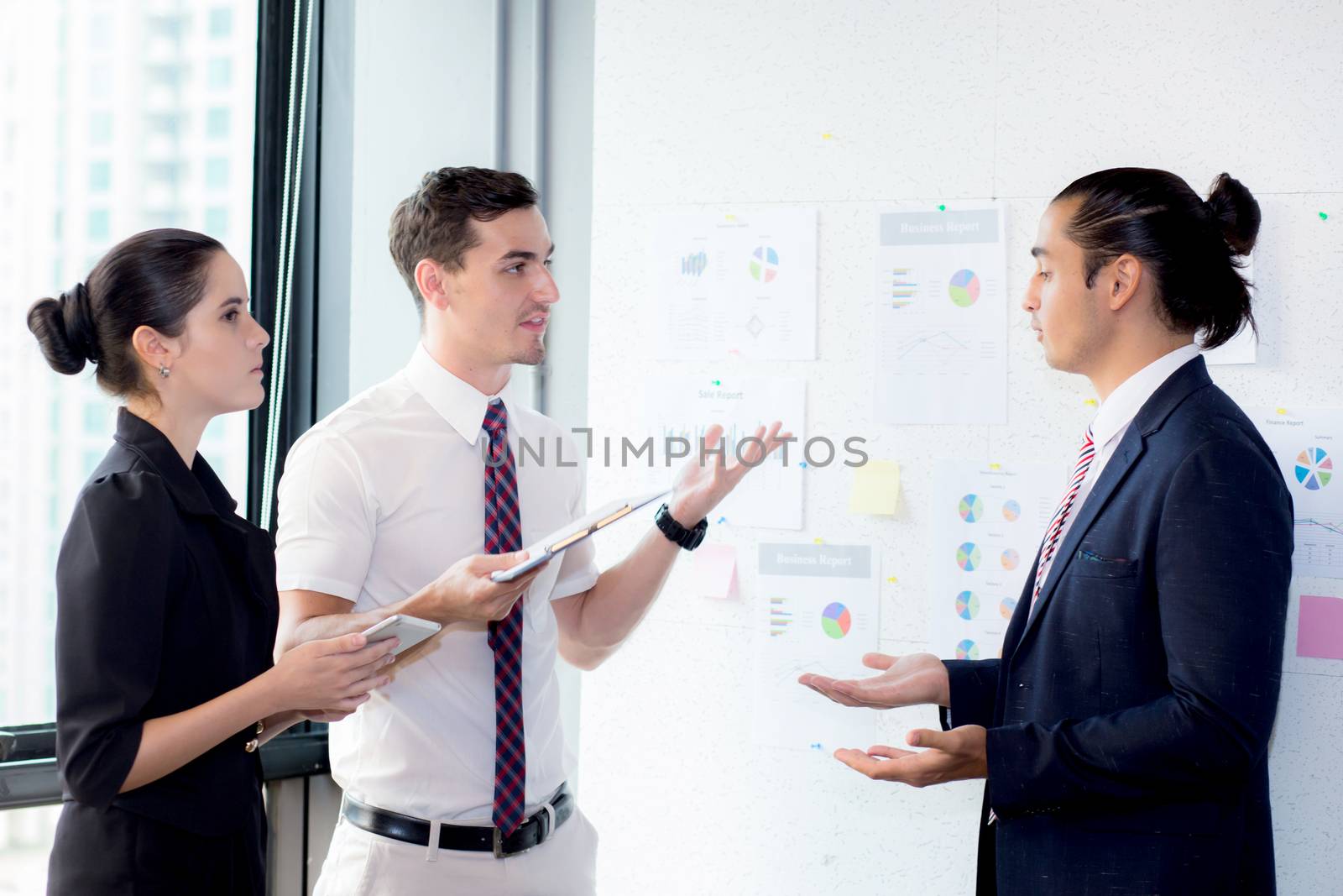 Three businesspeople standing in modern office looking file docu by nnudoo