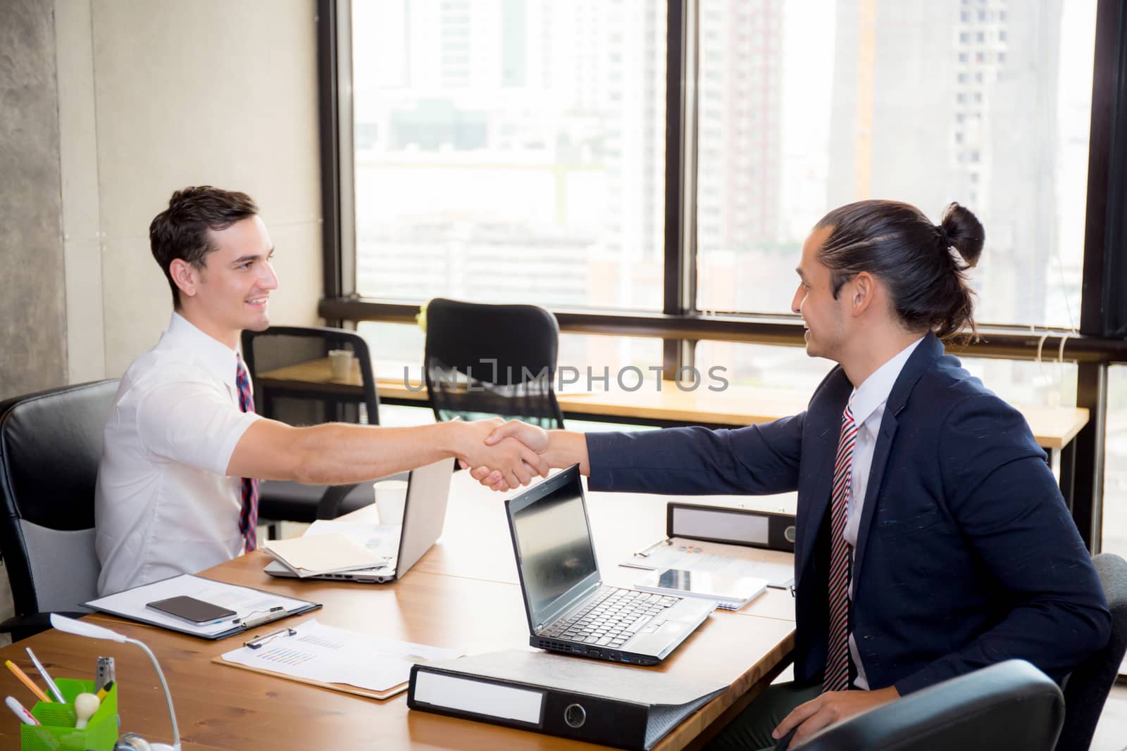 Two happy successful business partner shaking hands in the office.