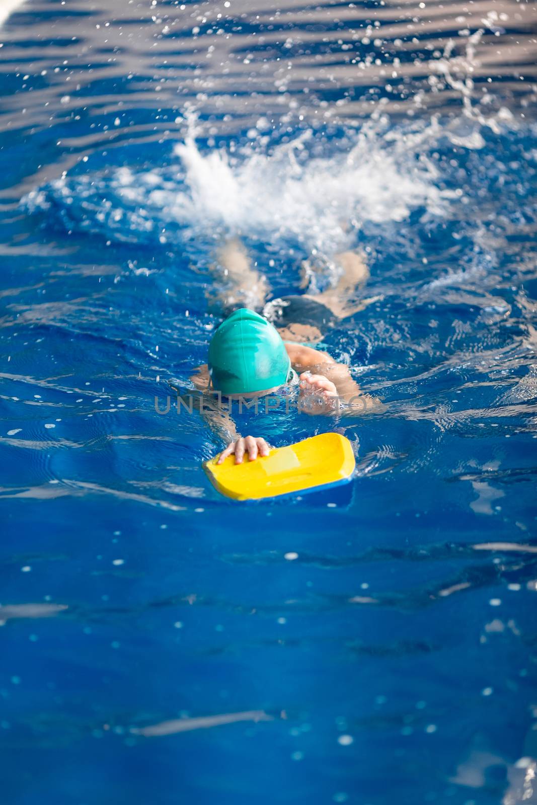 Cute little girl swimmer training in a swimming pool in glasses with a swimming kickboard. Swimming sport for kids concept