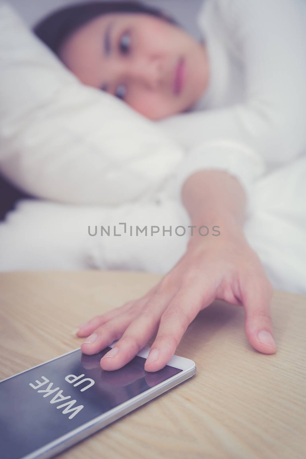 Hand of sleepy woman waking up with alarm clock on mobile phone in bedroom.