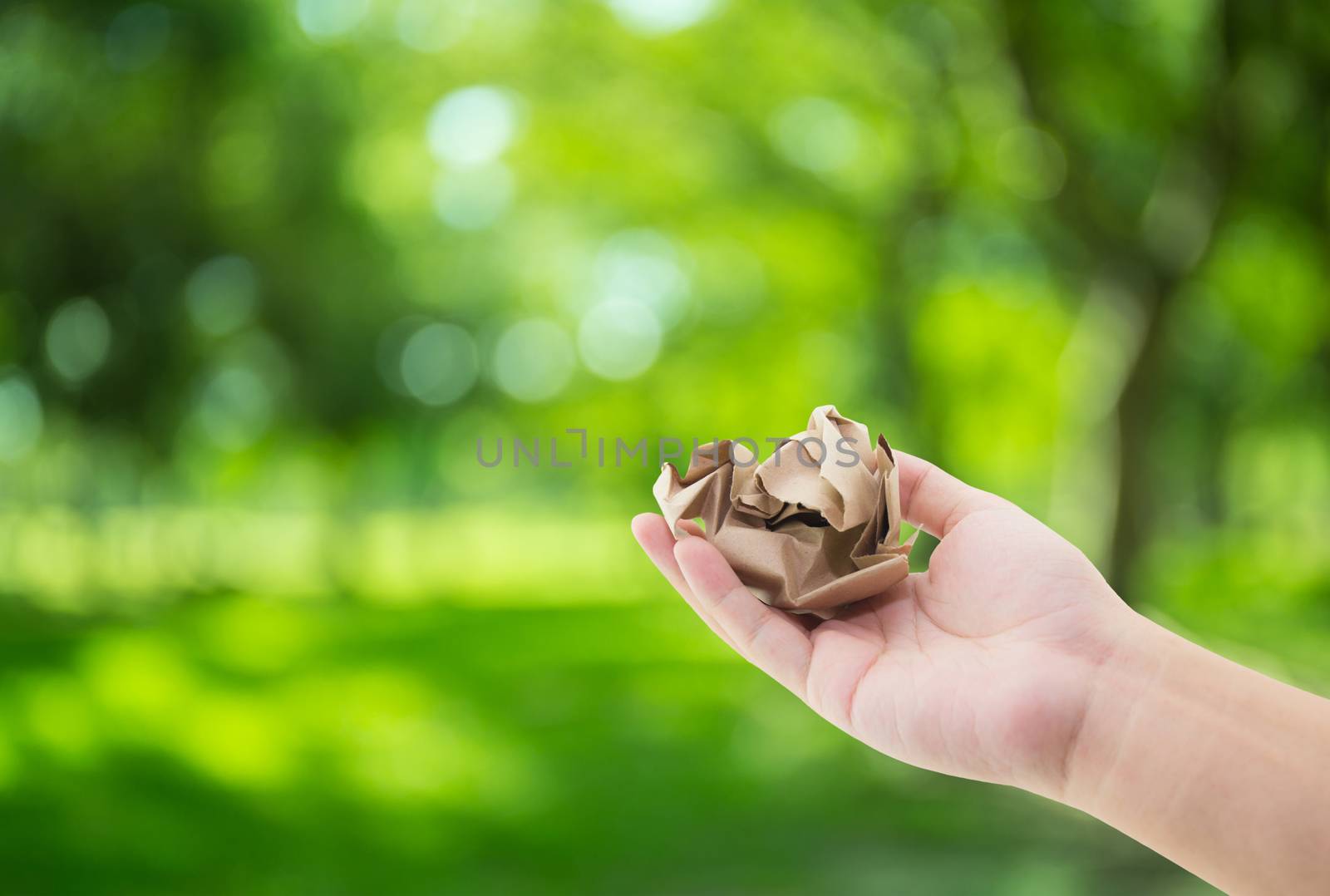 Hand holding crumpled paper on green nature background with environment concept.