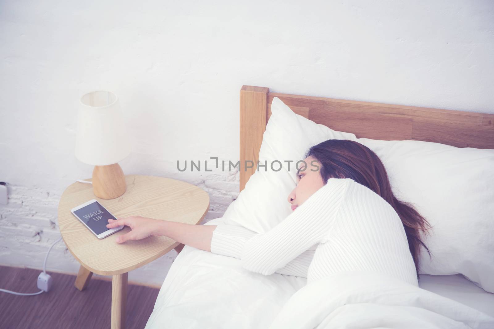 Hand of sleepy woman waking up with alarm clock on mobile phone in bedroom.