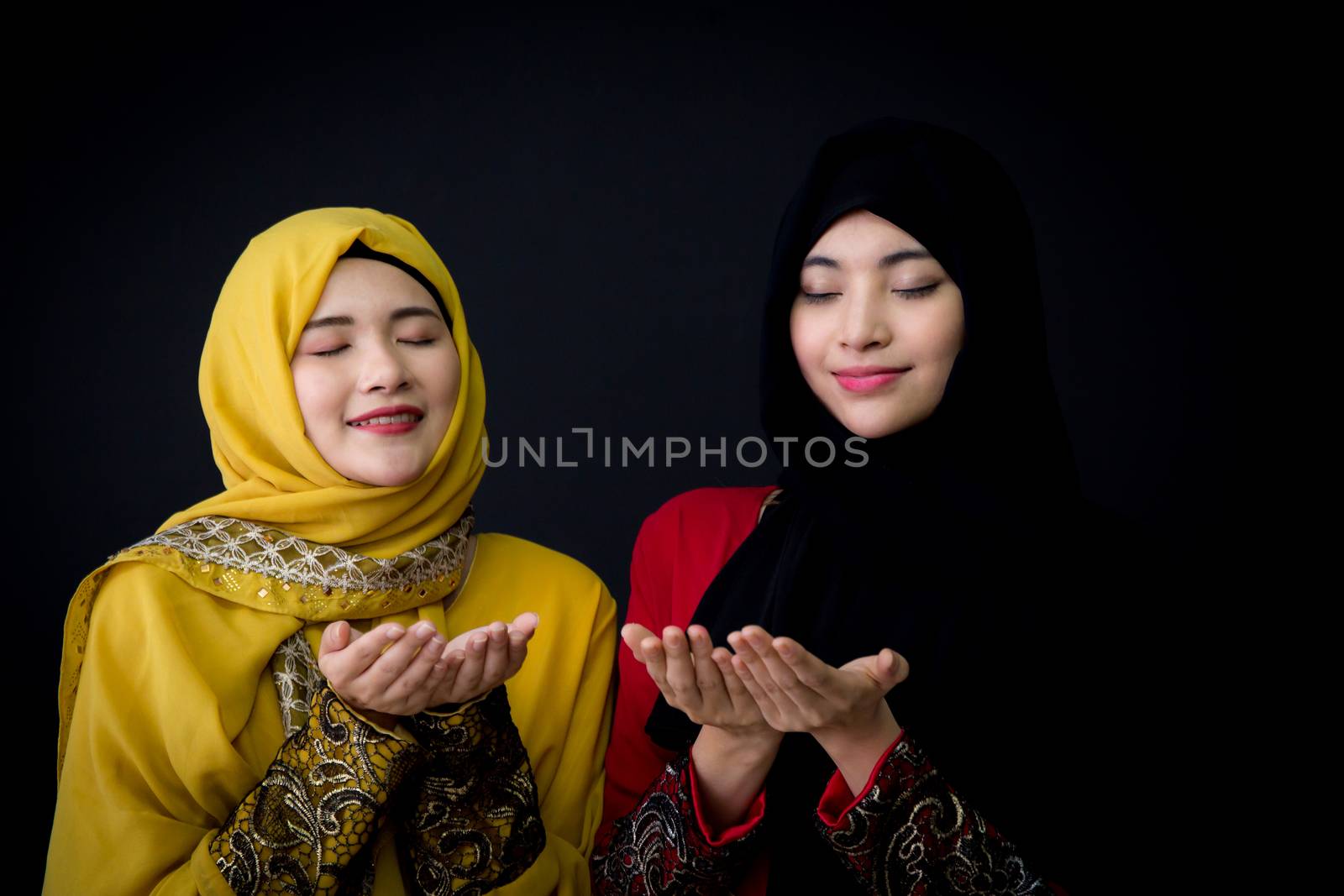 religious young Muslim two women praying over black background.